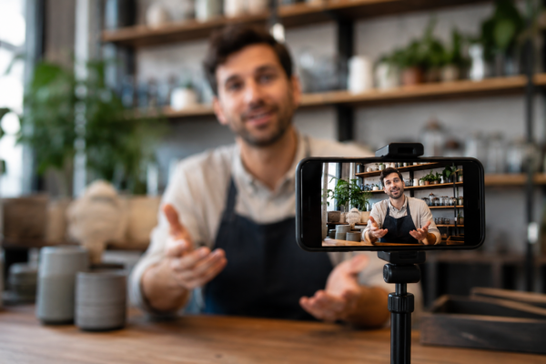 Entrepreneur filmé par un smartphone pour créer du contenu vidéo et renforcer la confiance des clients.